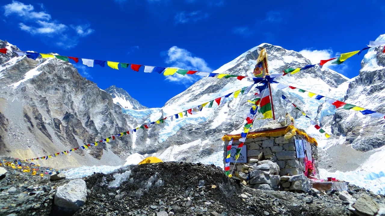 Le monument du camp de base de l’Everest, entouré de drapeaux de prières colorés, face à des sommets enneigés sous un ciel d’un bleu intense.